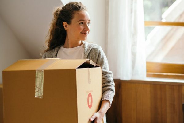 Junge Frau trägt einen Umzugskarton